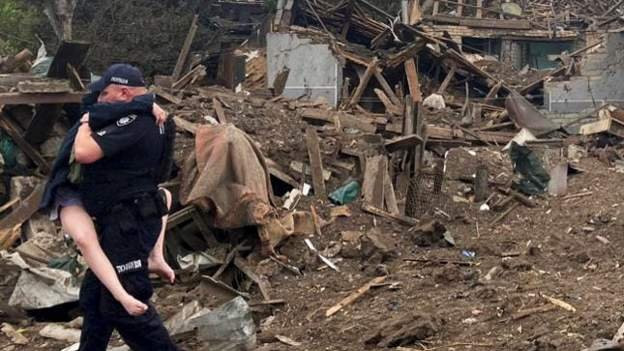 Policajac nosi dete iz uništene kuće u Kramatorsku