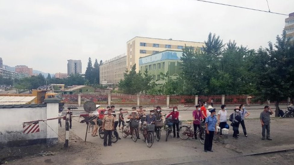 Masked citizens wait for a train to pass at a crossing in Phyongysong, North Korea