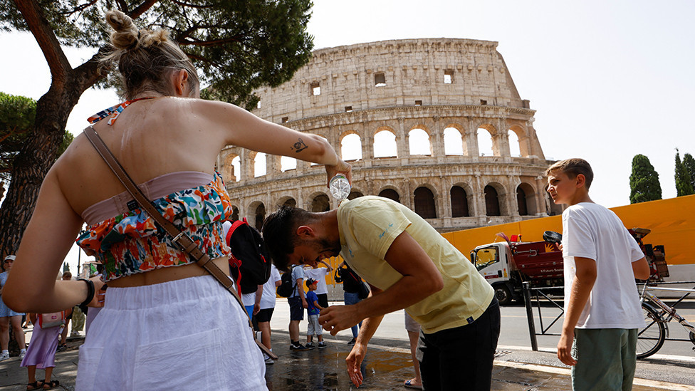 A woman pours water on a man near the Colosseum in Rome, Italy