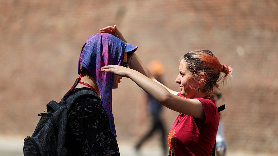 A woman puts a wet scarf on a man to protect him from the sun in Bologna, Italy