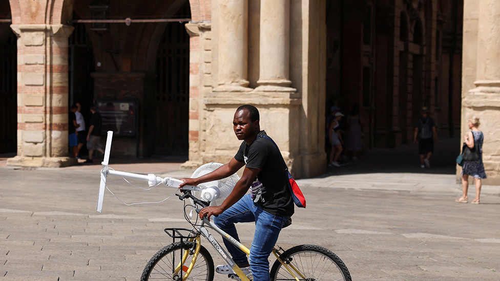 A man carries an electric fan with a bike in Bologna, Italy