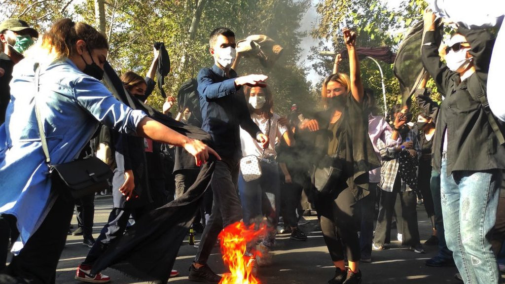 Iranian protesters set their scarves on fire while marching down a street on 1 October 2022 in Tehran