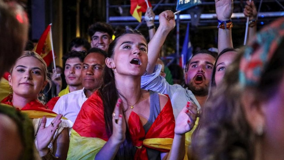 People wrapped in Spanish flags cheer in the street