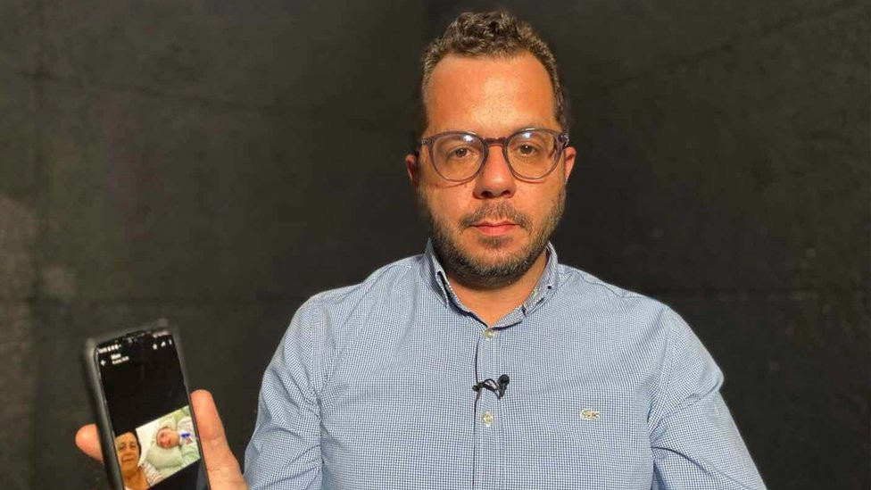 Elias Hayek holding his phone, showing an image of Lara in a hospital bed.