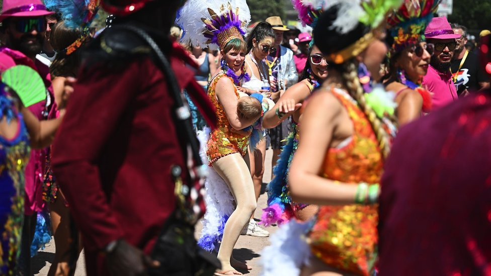 A dancer from a carnival samba band breastfeeds as they parade through the festival site on Day 4 of Glastonbury Festival 2023 on 24 June 2023 in Glastonbury, United Kingdom.