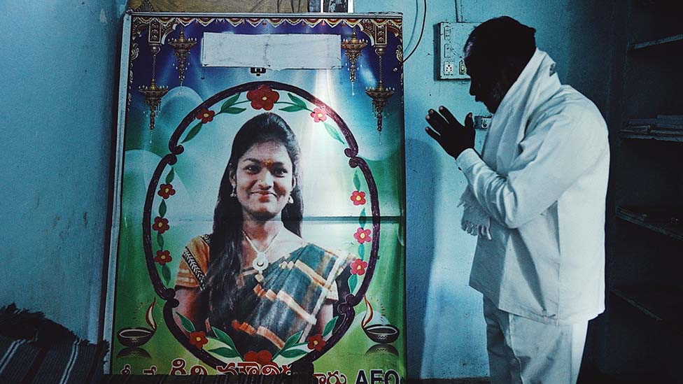 Mounika's father prays to a poster of her in her room