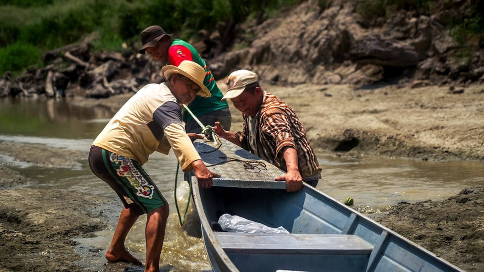 Oliveira and relatives tugging a canoe through a drying creek.