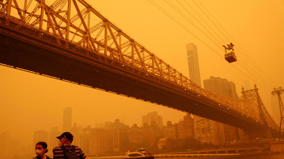 People wear protective masks as the Roosevelt Island Tram crosses the East River while haze and smoke from the Canadian wildfires shroud the Manhattan skyline in the Queens Borough New York City, U.S., June 7, 2023.