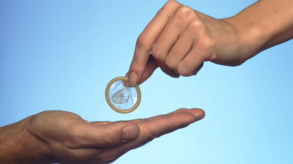 A woman's hand giving a condom to a man's hand