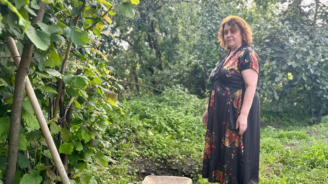 Irina's daughter Nino Elizbarashvili stands next to a suitcase and a shovel in the garden