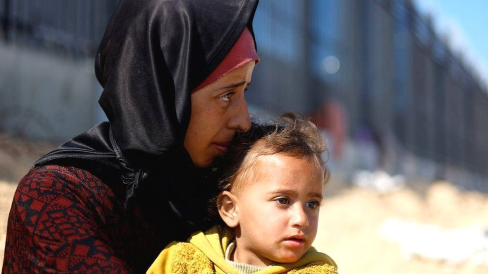 A woman sits with a child, as displaced Palestinians, who fled their houses due to Israeli strikes, take shelter in a tent camp amid the ongoing conflict between Israel and Hamas, near the border with Egypt in Rafah in the southern Gaza Stri