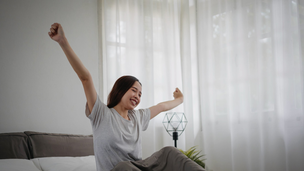 A woman stretches in bed in her own room.