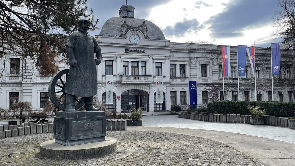 Spomenik Topolivcu ispred Upravne zgrade Zastave u Kragujevcu, na postamentu sadrži sliku radničkih demostracija od 27. februara 1876.