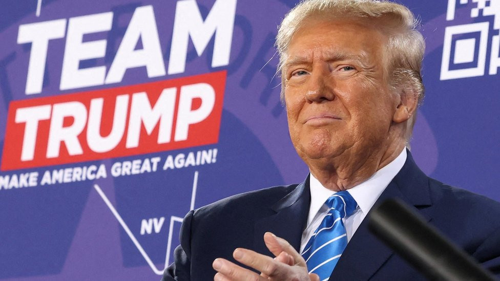 Donald Trump in front of a sign that reads "Team Trump"