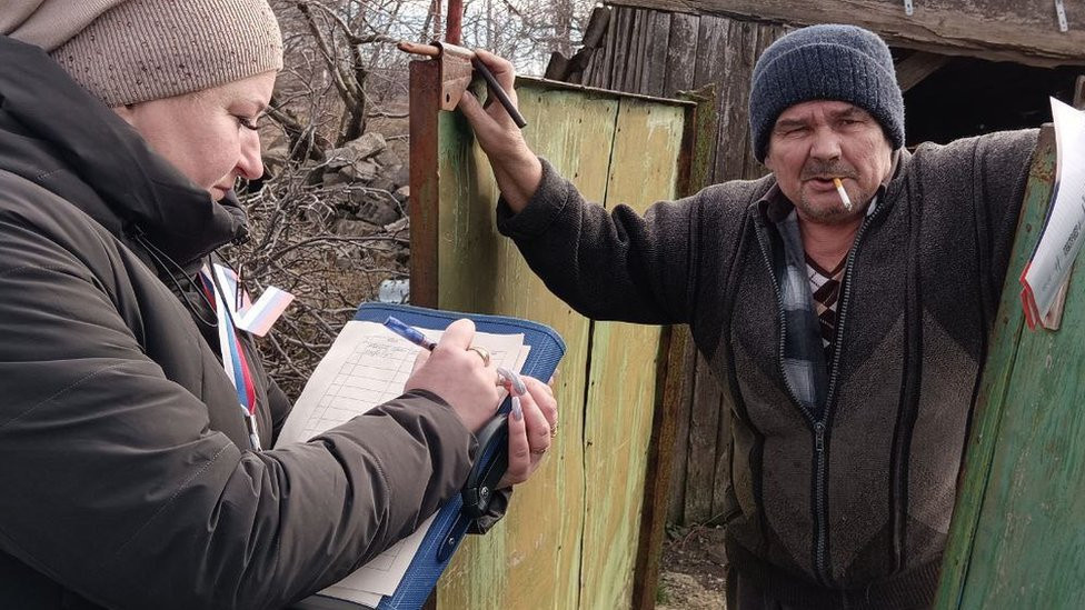 A woman with a clipboard gives a man in occupied Ukraine voting papers