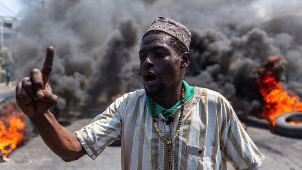 A man stands in front of an enormous plume of smoke as tyres burn