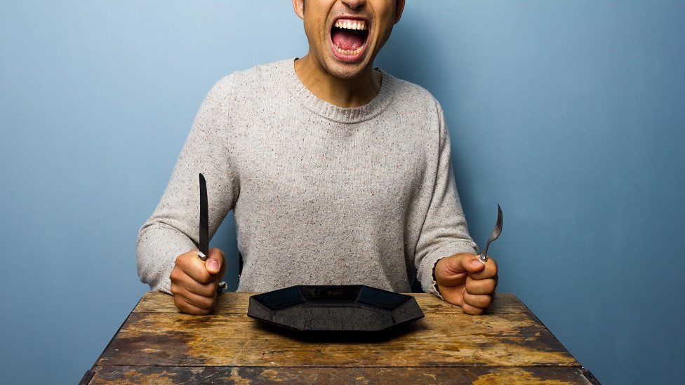 Hungry man sits at a table with plate, knife and fork