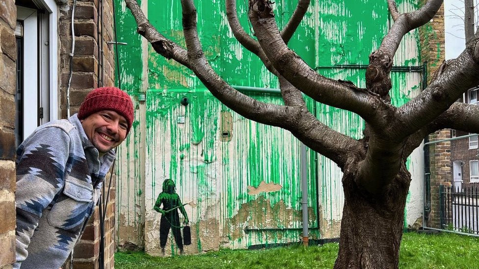 Carlos Serrano and the Bansky mural in Finsbury Park, London