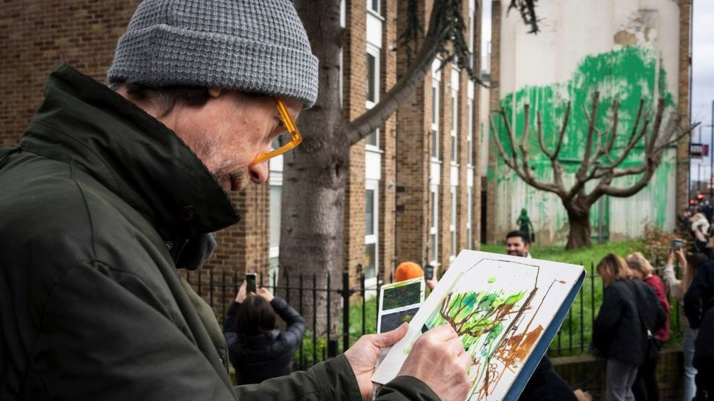 The Banksy mural from further away, where the green paint appears as foliage