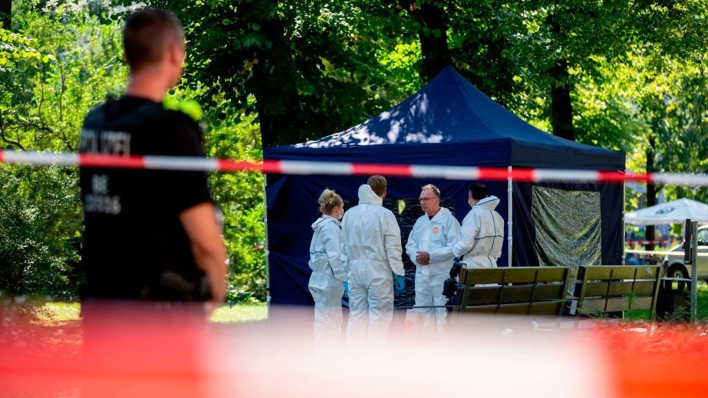 Police standing around a blue tent in a park over a dead body