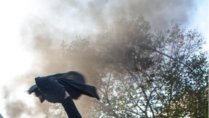 A woman without wearing a hijab beside other protesters gathers around burning dumpsters during a protest. The nationwide protests started after the death of Mahsa Amini, a 22-year-old girl who died under the custody of the Islamic Republic's Morality Police on September 16th, 2022 in Tehran, Iran.