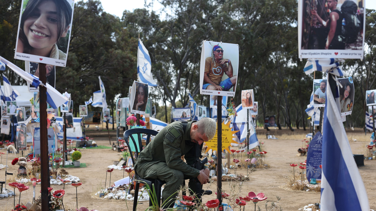 Izraelski vojnik sedi na stolicipognute glave među cvećem na mestu gde je Hamas ubio učesnike festivala