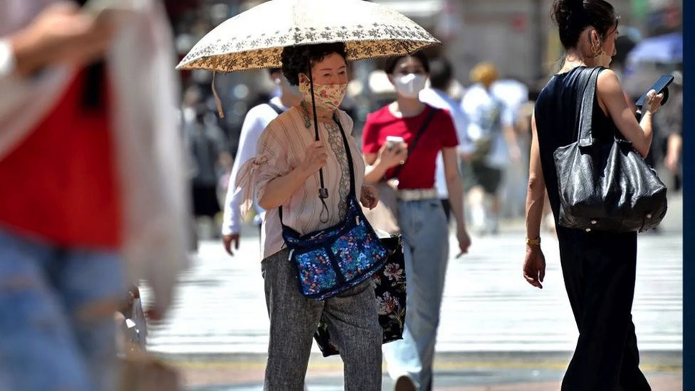 Japanka šeta gradom sa ručnim suncobranom i maskom na licu