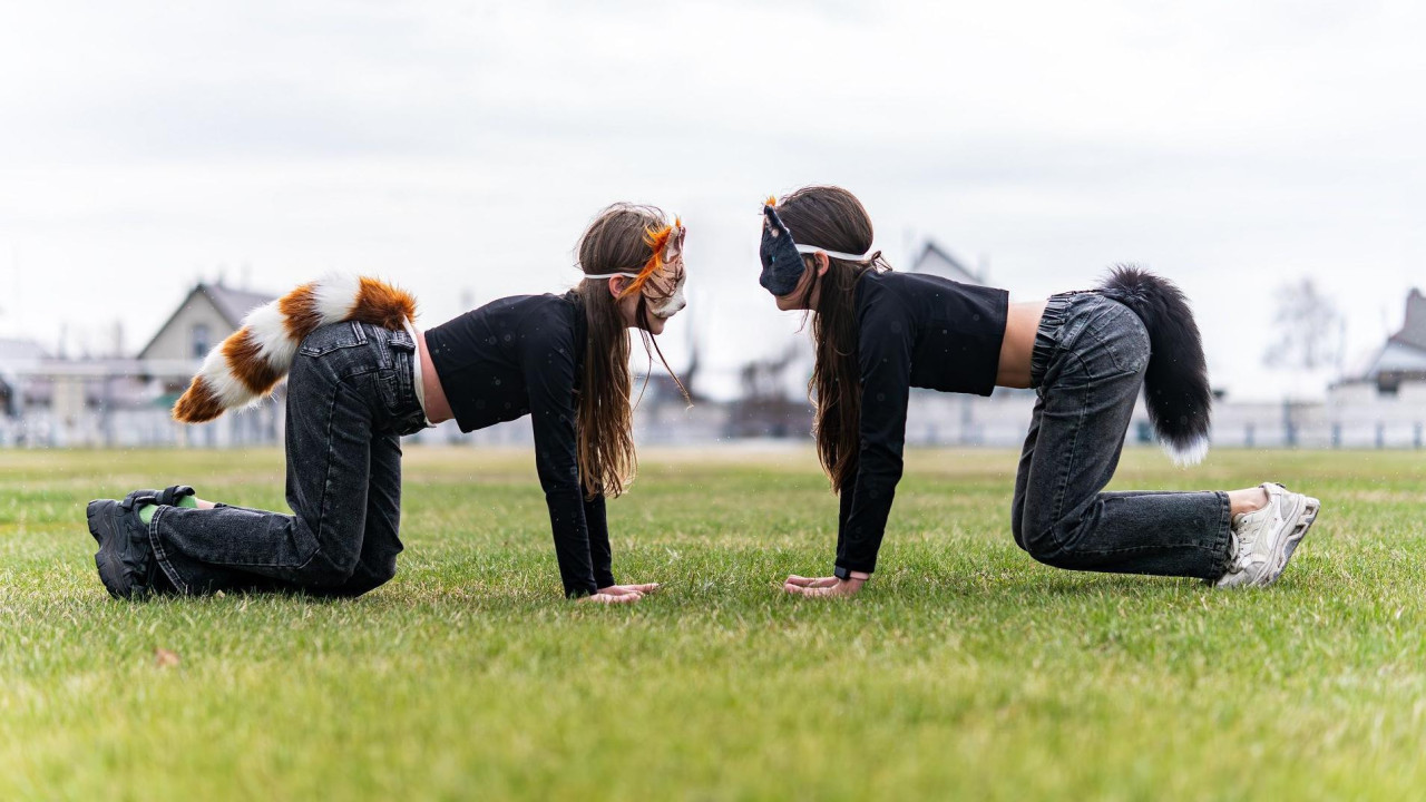 Dve tinejdžerke sa maskama životinja na licu i repovima kleče oslonjene rukama na zemlju