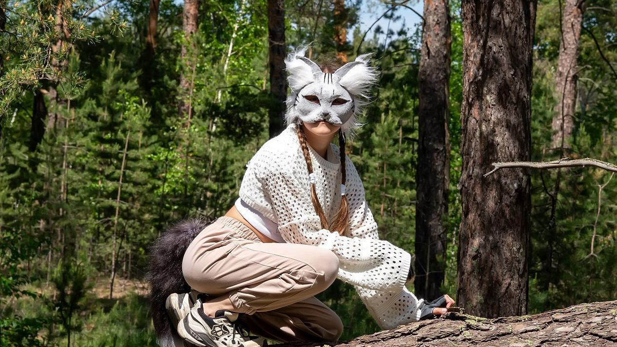 Tinejdžerka nosi masku životinje na glavi i čuči na oborenom drvetu
