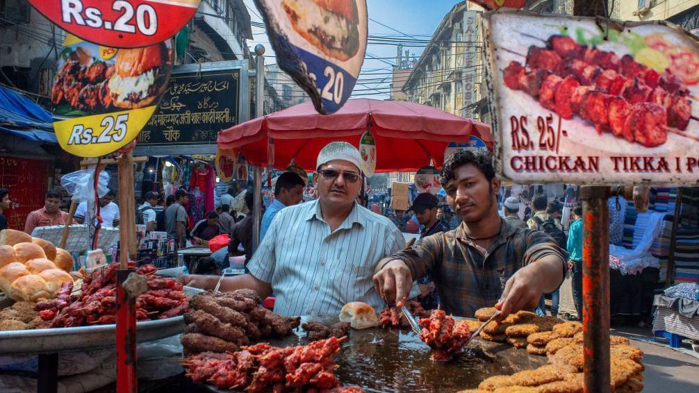 Dva muškarca stoje pored velikih metalnih štandova sa kuvanim mesom, u Mumbaiju, 2022.