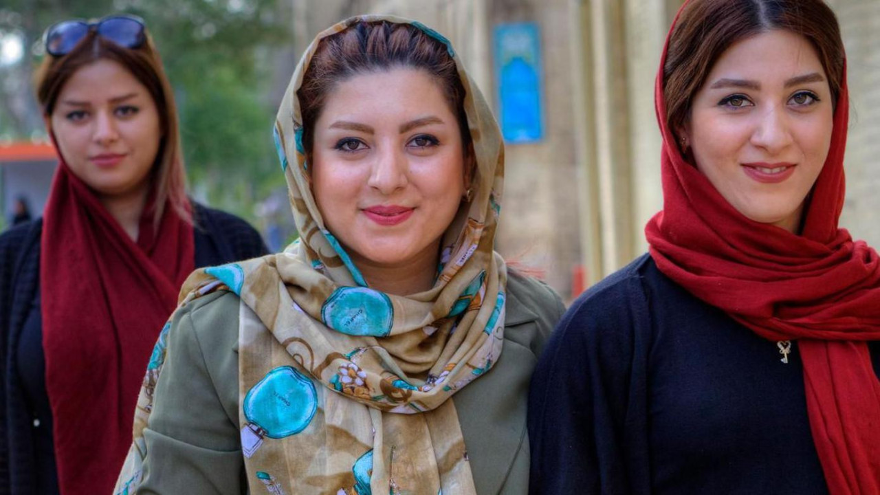 Mlade Iranke, obučene u hidžab, šetaju gradskom ulicom sa  mobilnim telefonima u rukama.