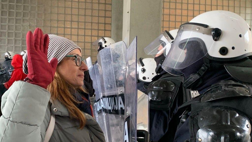 Žena sa podignutim rukama ispred policajca pod punom opremom za razbijanje demonstracija