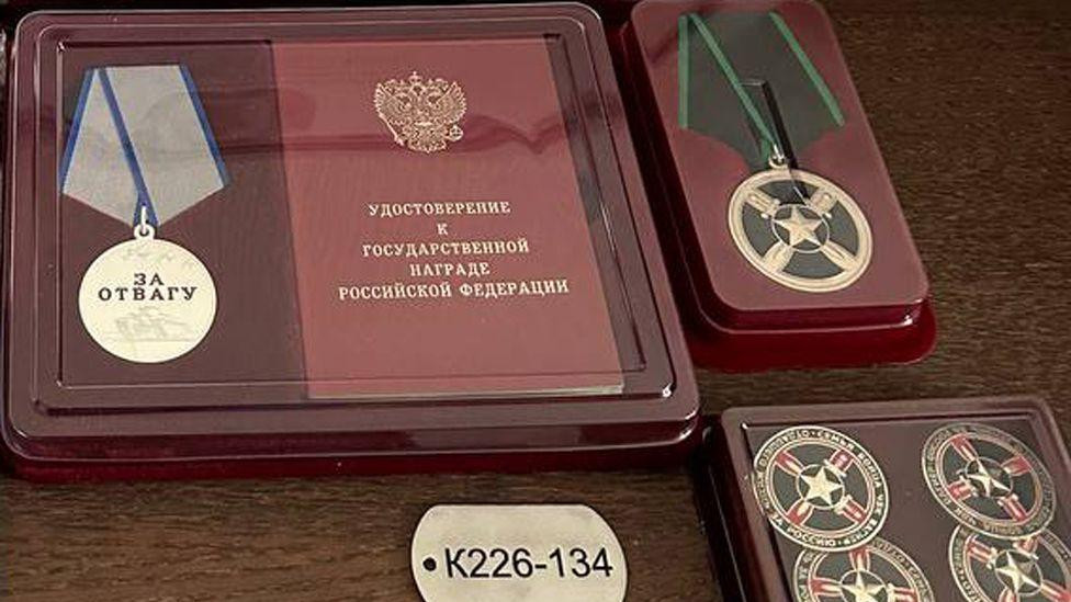 Identifikaciona pločica na kojoj piše  „K226-134" i medaljana kojoj je ugravirano „za hrabrost"  