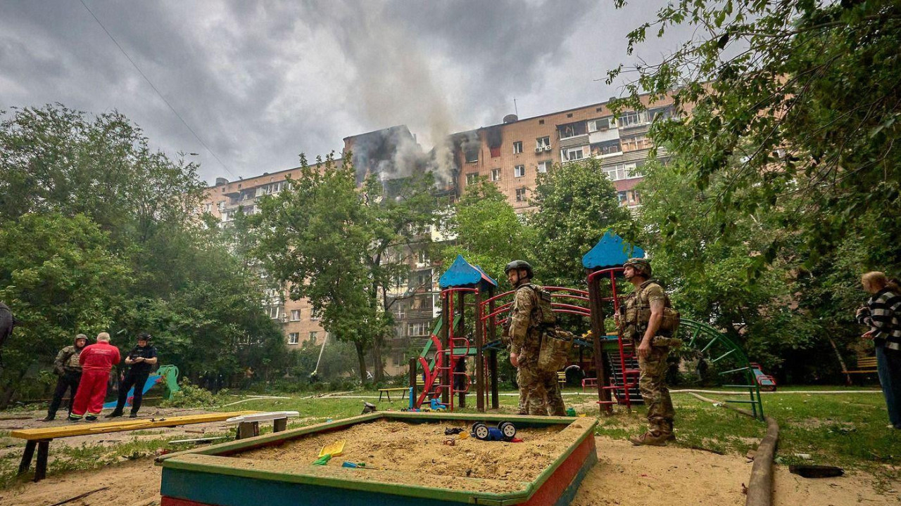 Vojnici i ljudi stoje na igralištu. Iza njih gori zgrada