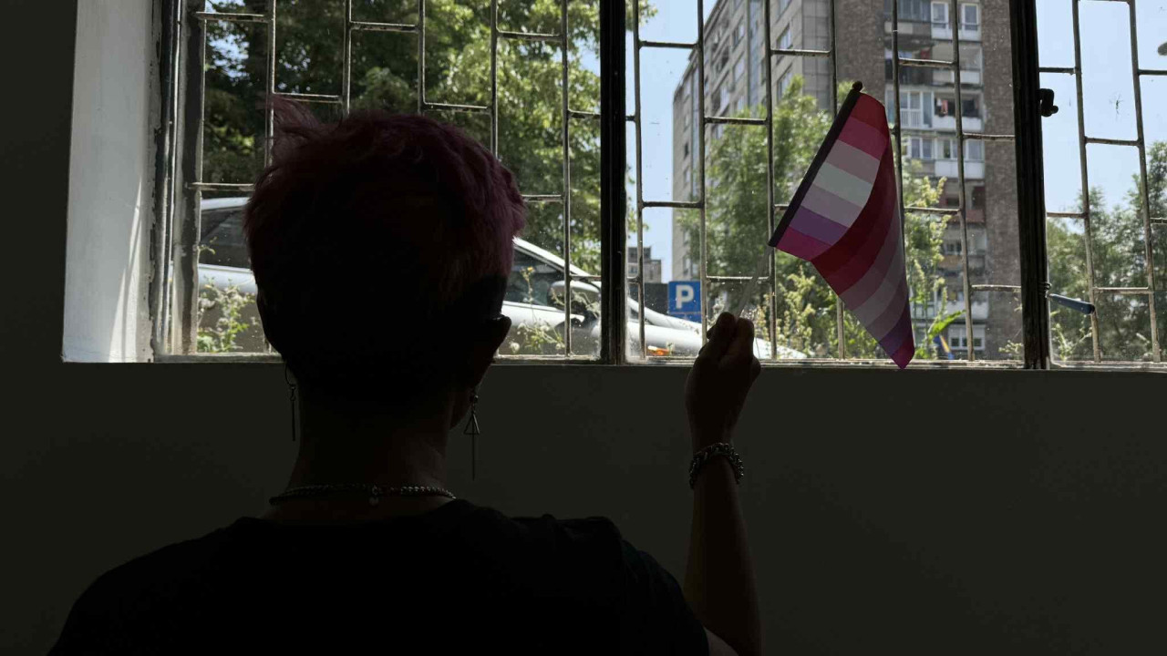 Devojka sa kratkom kosom gleda napolje i drži zastavu u ruci