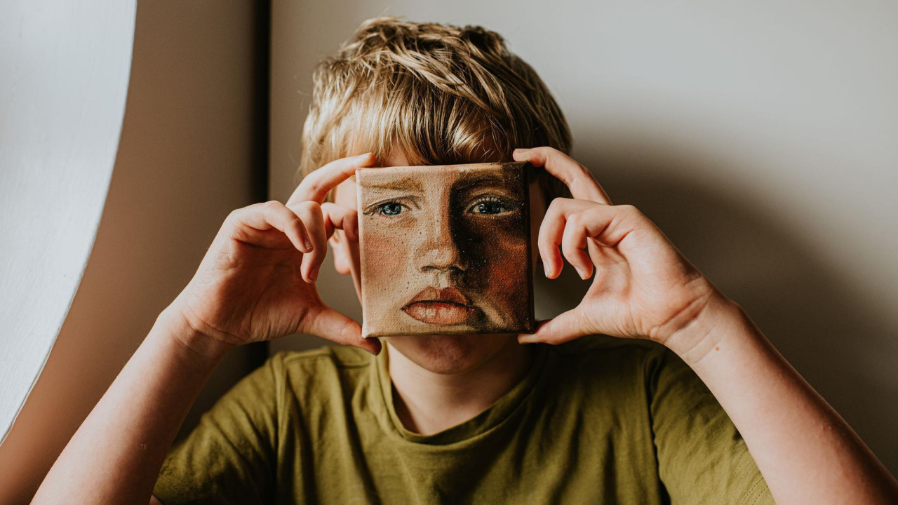 Dečak drži uljani portret lica preko svog lica