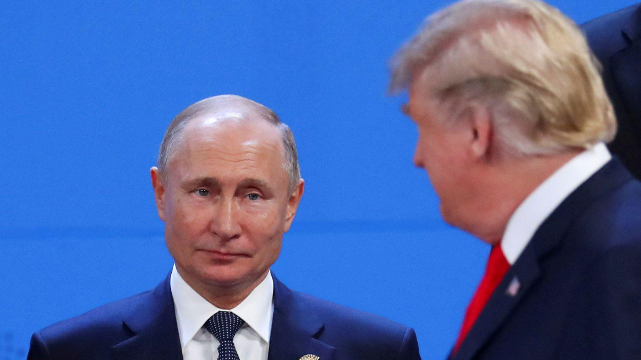 Vladimir Putin, who has thinning grey hair and wears a navy suit, white shirt and navy polka dot tie, looks toward Donald Trump, who has blonde hair combed to the side and wears a navy suit with a white shirt and red tie, at the G20 leaders summit in 2018