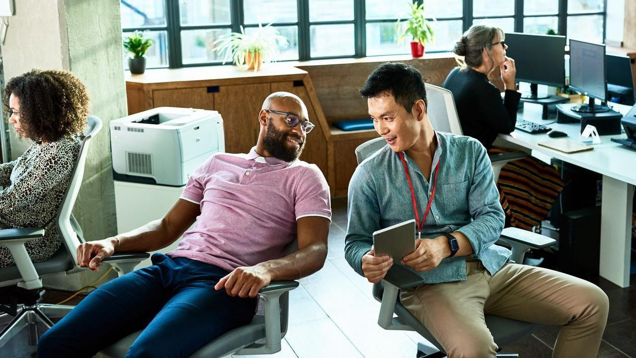 Dva muškarca sede u radnim stolicama i pričaju