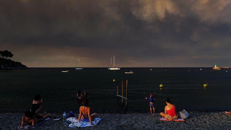 Turisti na plaži na jugu Francuske dok se gust dim izdiže iznad mora
