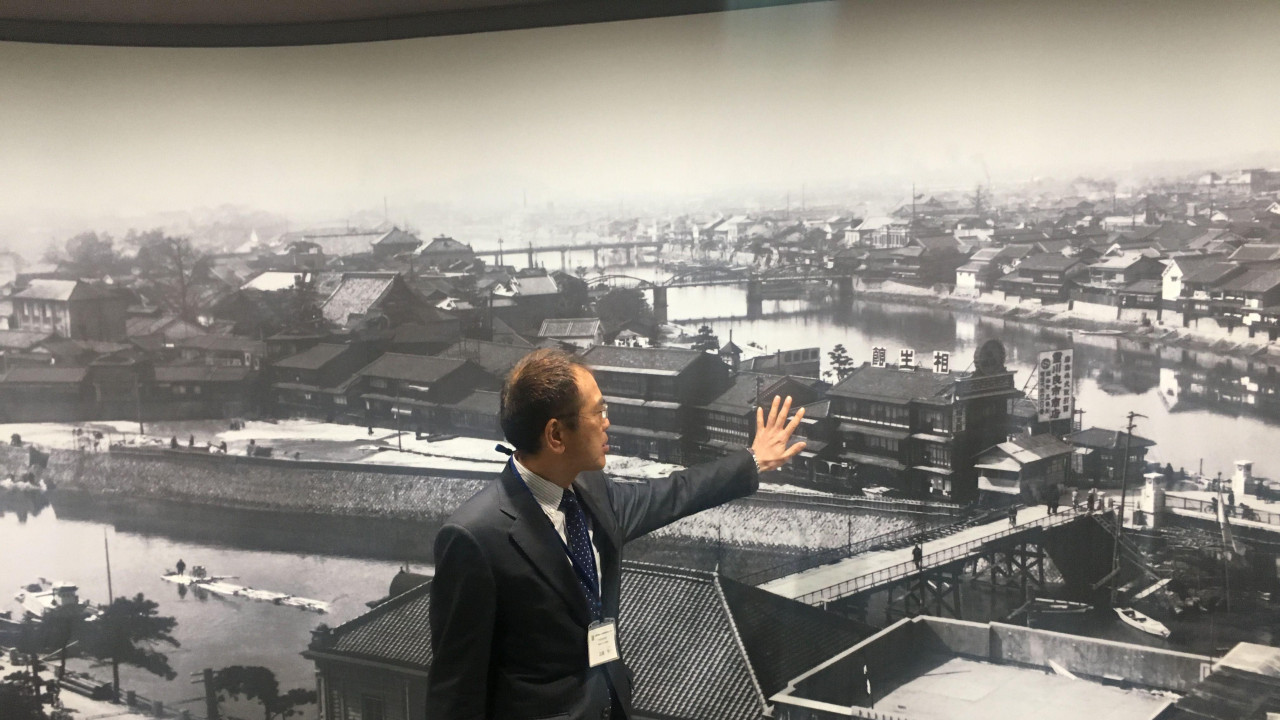 Muškarac rukom pokazuje na fotografiju Hirošime pre bombardovanja 