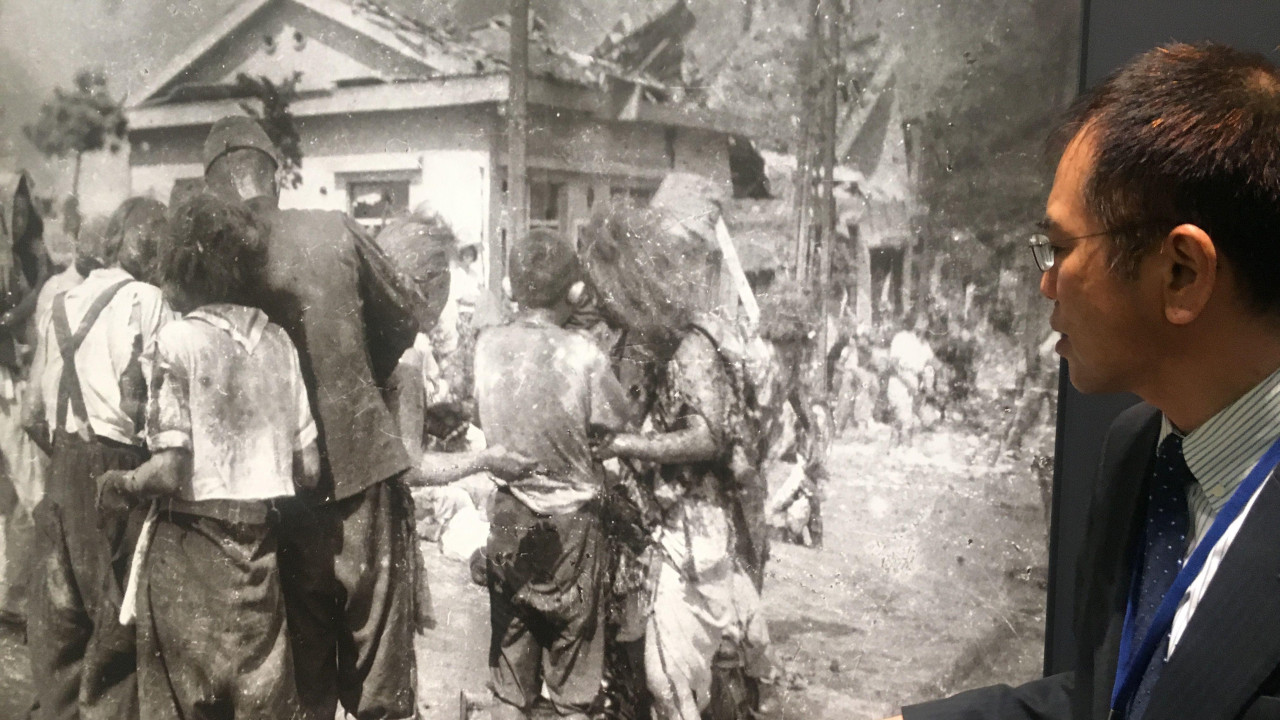 Muškarac stoji pored fotografije dece koja stoje u gomili posle atomske bombe u Hirošimi