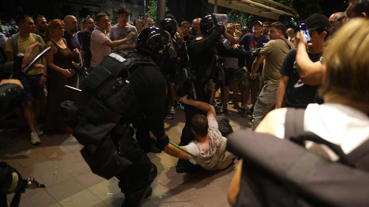 Policajac vuče demonstranta na ulici po noći, okruženi su drugim demonstrantima