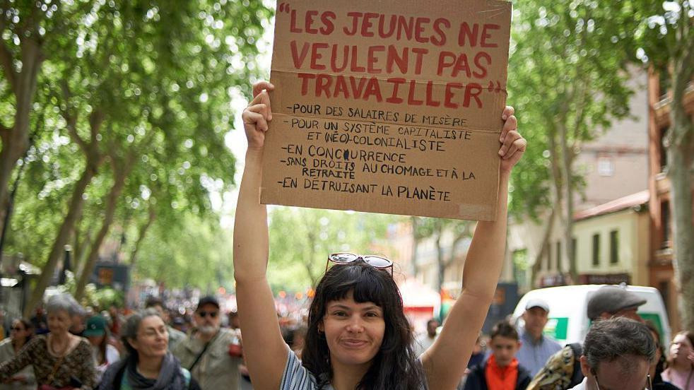 Devojka drži transparent sa porukom: Mladi ne žele više da rade za malu platu, kapitalizam i neokolonijalni sistem bez prava na penziju i beneficije