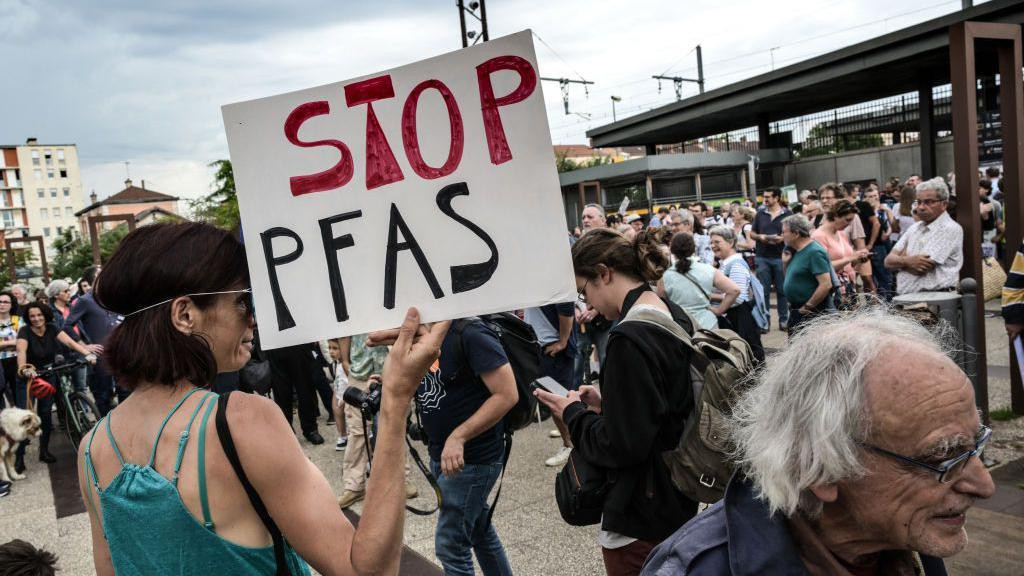 Žena na demonstracijama okružena ljudima drži transparent u ruci