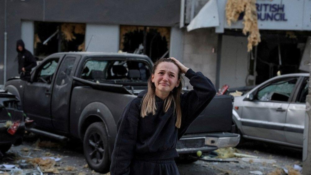 napoad na kijev, žena uplakana posle ruskog napada na kijev, iza je pogođena zgrada 