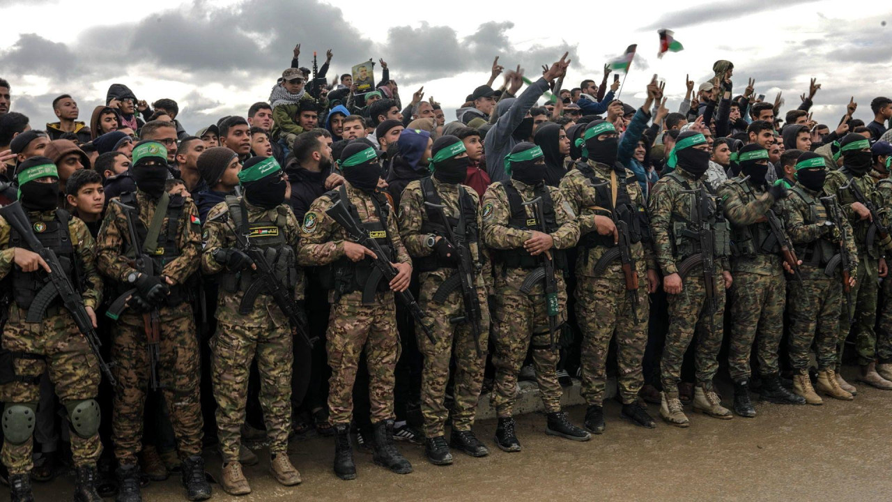 Red naoružanih boraca Hamasa stoji leđima okrenut prema gomili ljudi u civilnoj odeći.