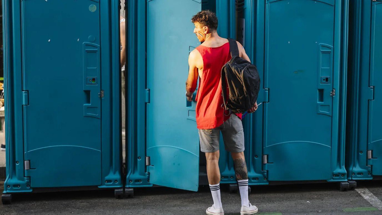 Muškarac stoji ispred pokretnog toaleta na ulici