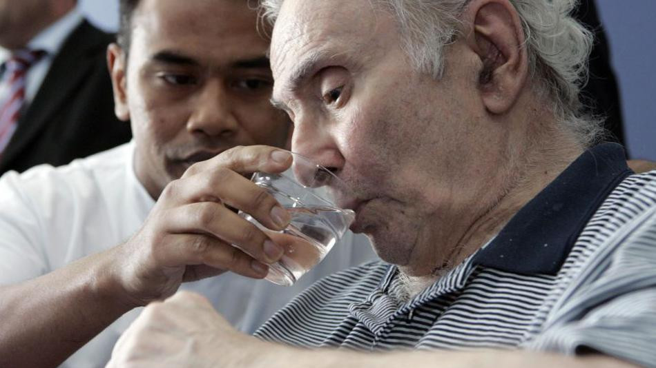 Negovatelj pažljivo daje veoma bledom starijem čoveku čašu vode