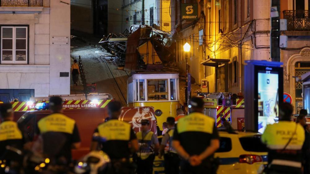 Police officers look at the wreckage of the Lisbon's Gloria funicular railway car that derailed and crashed