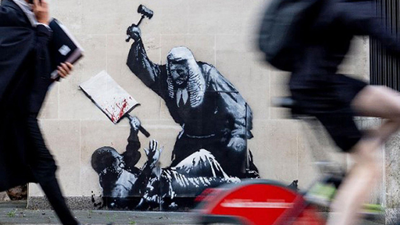 A member of the legal profession walking past a Banksy mural on the walls of the Royal Courts of Justice